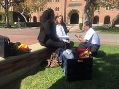 Three people sitting on a wall with luggage.