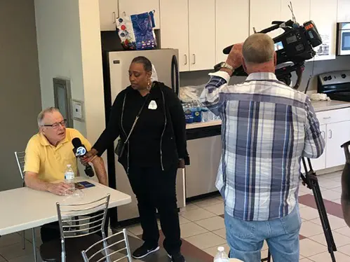 A man is filming two people in the kitchen.