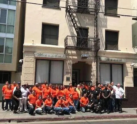 A group of people in orange shirts standing on the side walk.